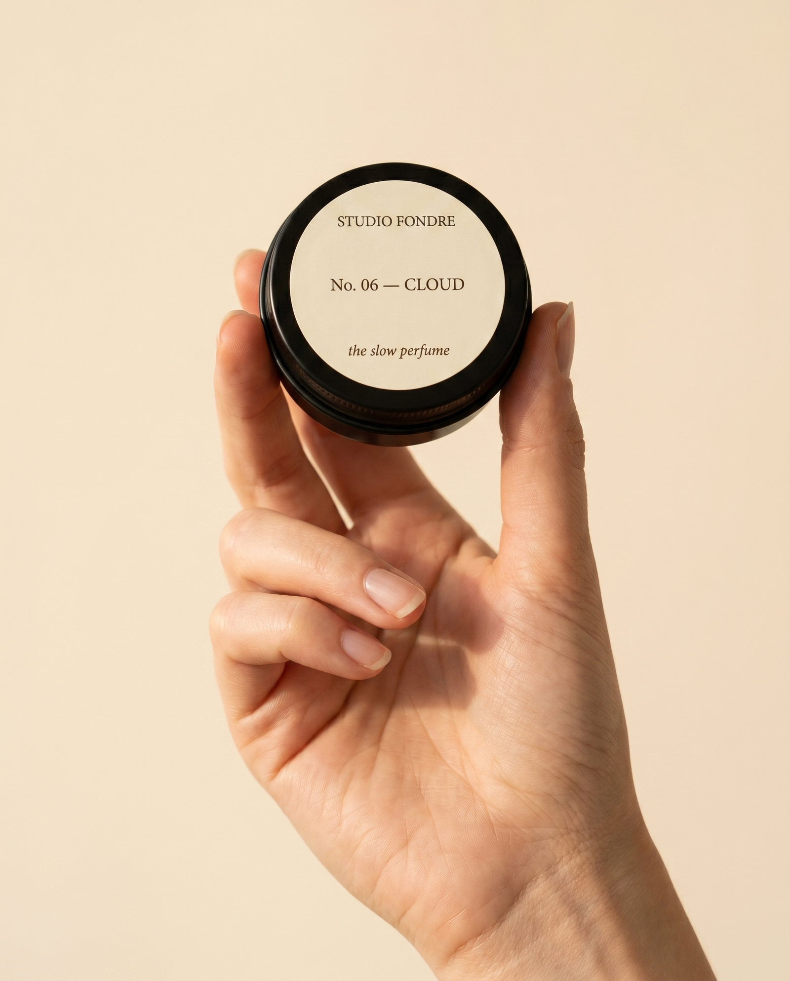 Solid perfume tin held between fingers, showing pocket-sized scale